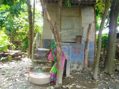 A woman indicates the last flood water levels that inundated the Kairi village. The toilet was still accessible [image by: Aparna Unni]