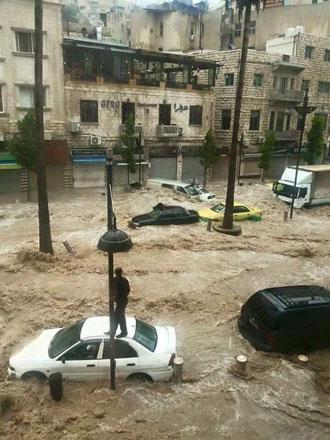 An Amman, Jordan, resident stands on top of his car as floodwaters surround other vehicles in the neighborhood. 